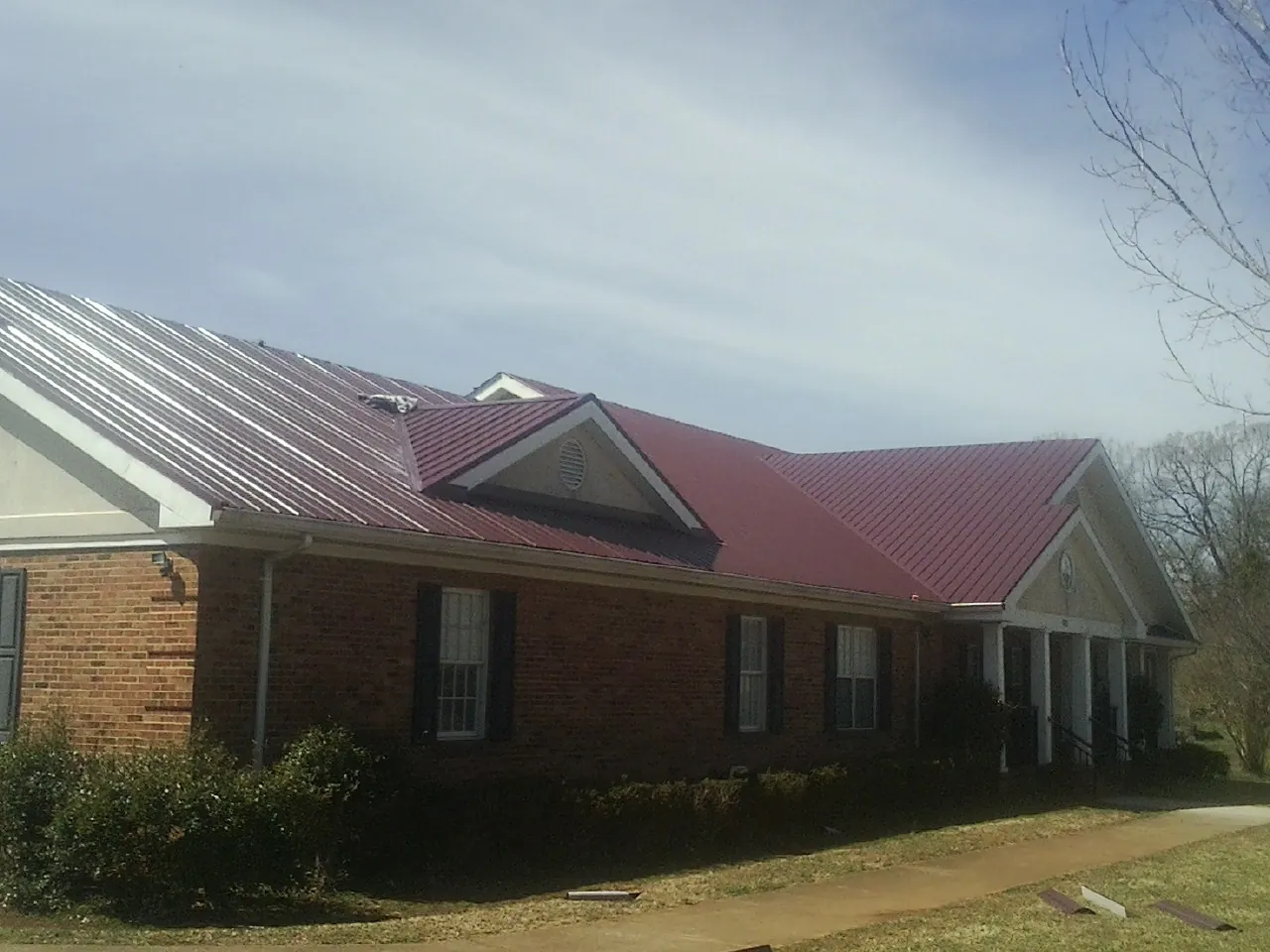 Red metal roof with gabled entries on a long brick building, from a Hail Damage Roof Repair job in Toulon